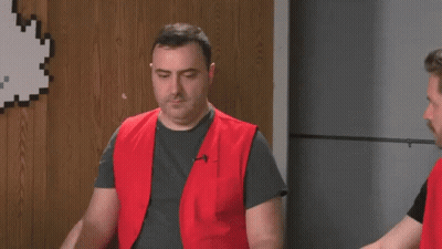 A Man In A Red Vest Is Standing Next To Another Man In A Gray Shirt . GIF