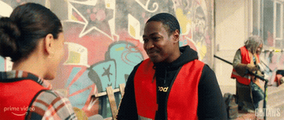 A Man In A Red Vest Talking To A Woman In Front Of A Graffiti Wall . GIF