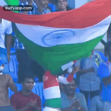 A Man In A Red , White And Green Shirt Is Holding A Flag In A Crowd Of People . GIF