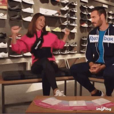 A Man In A Reebok Jacket Sits Next To A Woman On A Bench In A Store GIF