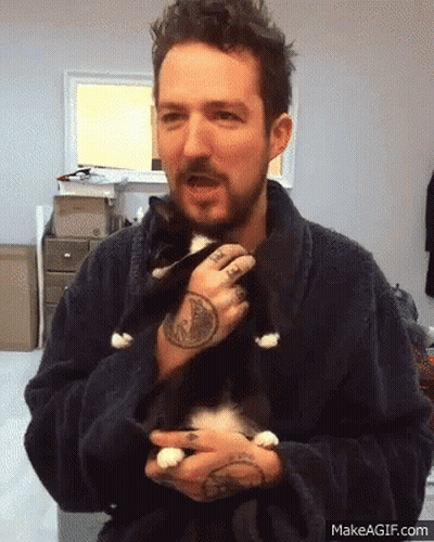 A Man In A Robe Is Holding A Black And White Cat In His Arms GIF
