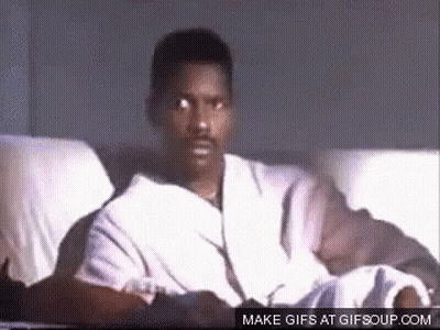 A Man In A Robe Is Sitting On A Couch And Looking At The Camera . GIF
