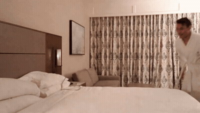 A Man In A Robe Is Standing In A Hotel Room GIF
