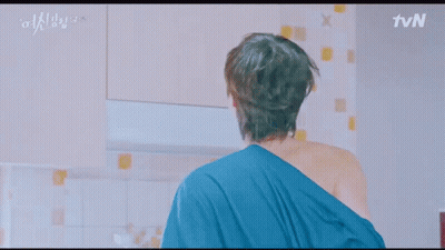 A Man In A Robe Is Standing In A Kitchen With A Microwave And A Refrigerator . GIF