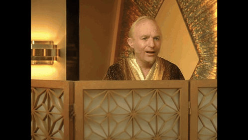 A Man In A Robe Stands Behind A Wooden Partition GIF