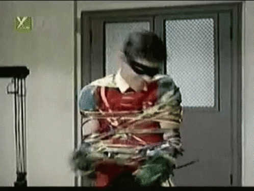 A Man In A Robin Costume Is Tied Up With A Rope In A Room . GIF