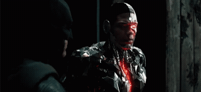 A Man In A Robotic Suit Is Standing Next To A Man In A Batman Hat . GIF