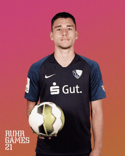 A Man In A Ruhr Games Shirt Holds A Soccer Ball In His Hands GIF