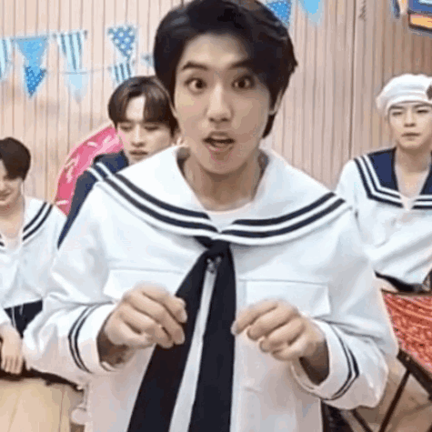 A Man In A Sailor Suit And Tie Is Standing In Front Of A Group Of Young Men . GIF