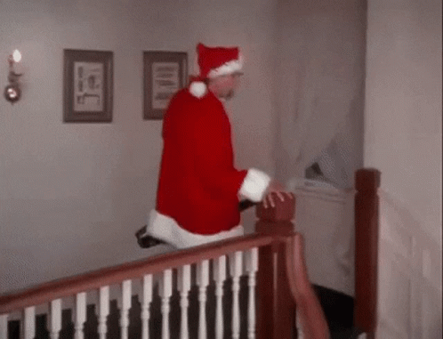 A Man In A Santa Claus Costume Is Walking Down A Set Of Stairs . GIF