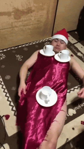 A Man In A Santa Hat Is Laying On The Floor With Cups And Saucers GIF