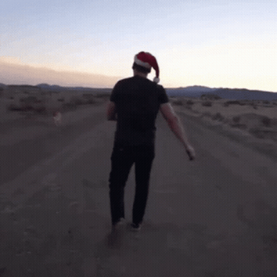 A Man In A Santa Hat Is Walking Down A Dirt Road GIF