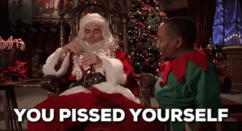 A Man In A Santa Suit Is Sitting In A Chair Next To A Man In A Green Sweater . GIF