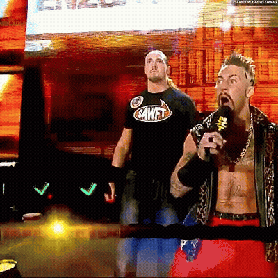 A Man In A Sawfit Shirt Stands Next To Another Man GIF