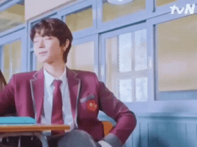 A Man In A School Uniform Is Sitting At A Desk In A Classroom . GIF