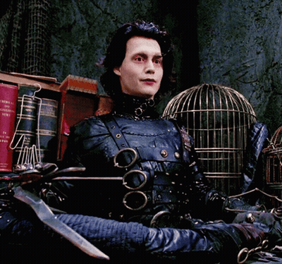 A Man In A Scissors Costume Is Sitting In Front Of A Cage GIF