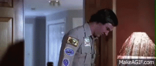 A Man In A Scout Uniform Is Standing In Front Of A Lamp In A Room . GIF