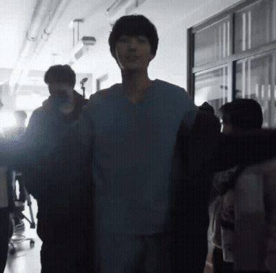 A Man In A Scrub Top Is Standing In A Hallway With A Group Of People GIF