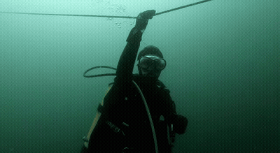 A Man In A Scuba Suit Is Holding A Rope In The Water . GIF
