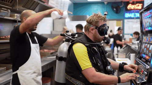 A Man In A Scuba Suit Is Playing A Slot Machine In A Restaurant GIF