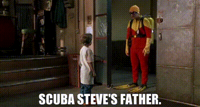A Man In A Scuba Suit Is Standing Next To A Boy In A White Shirt And Talking To Him . GIF
