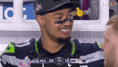A Man In A Seahawks Jersey Is Smiling While Watching A Game GIF