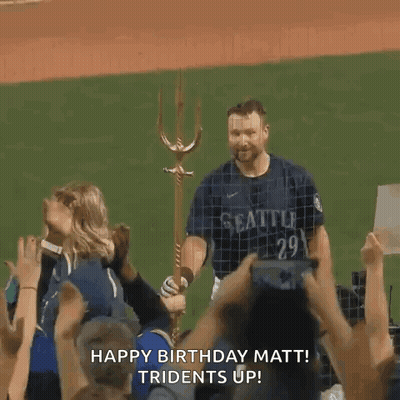 A Man In A Seattle Jersey Is Standing On A Baseball Field With A Trident In His Hand . GIF