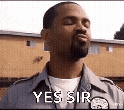 A Man In A Security Uniform Is Standing In Front Of A Building With His Eyes Closed And Saying Yes Sir . GIF