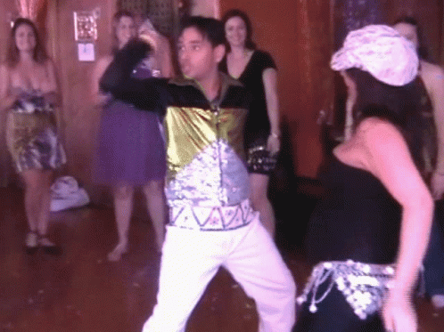 A Man In A Sequined Shirt Is Dancing With A Woman GIF