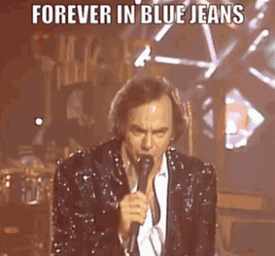 A Man In A Sequined Suit Is Singing Into A Microphone On Stage . GIF