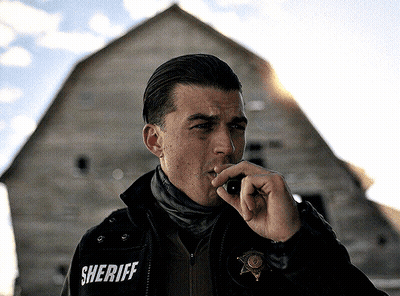 A Man In A Sheriff 'S Jacket Talks On A Walkie Talkie GIF