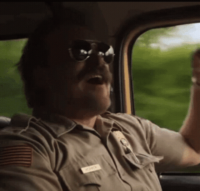 A Man In A Sheriff 'S Uniform And Sunglasses Is Driving A Car . GIF
