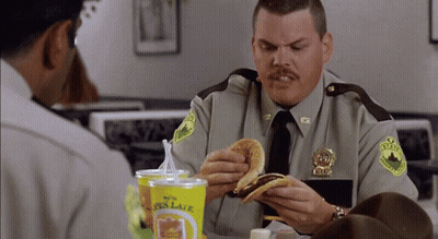 A Man In A Sheriff 'S Uniform Eating A Burger GIF