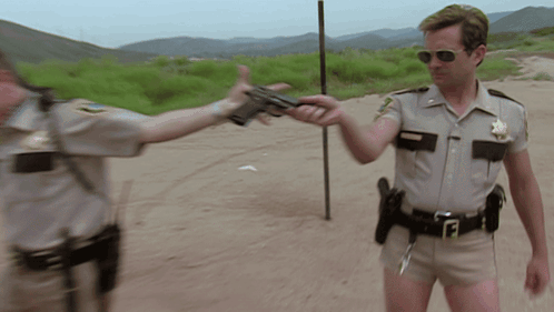 A Man In A Sheriff 'S Uniform Holds A Gun To Another Man GIF