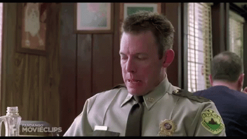 A Man In A Sheriff 'S Uniform Is Sitting At A Table In A Restaurant Eating Food . GIF