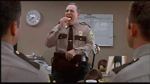 A Man In A Sheriff 'S Uniform Stands In Front Of A Clock That Shows The Time As 7:20 GIF