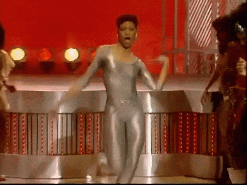 A Man In A Silver Leotard Is Dancing On A Stage GIF
