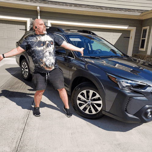 A Man In A Skull Shirt Stands In Front Of A Subaru GIF