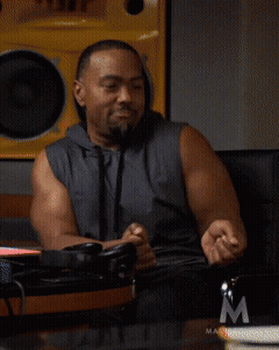 A Man In A Sleeveless Hoodie Is Sitting In Front Of A Masterclass Logo GIF