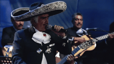 A Man In A Sombrero Sings Into A Microphone While Another Man Plays Guitar GIF