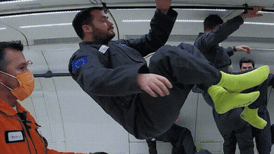 A Man In A Space Suit Is Being Lifted In The Air By A Man Wearing A Mask GIF
