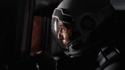 A Man In A Space Suit Is Smoking A Cigarette In A Room . GIF