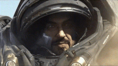 A Man In A Space Suit Looks At The Camera With His Hand On His Chin GIF
