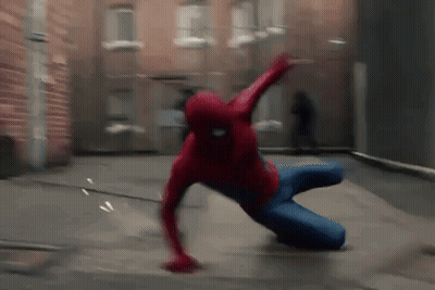A Man In A Spiderman Costume Is Crawling On The Ground In Front Of A Brick Building . GIF