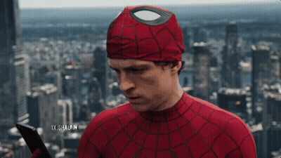 A Man In A Spiderman Costume Is Holding A Cell Phone In Front Of A City Skyline GIF