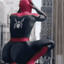 A Man In A Spiderman Costume Is Squatting Down In Front Of A Tall Building . GIF