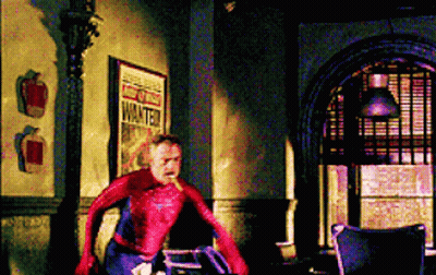 A Man In A Spiderman Costume Is Standing In A Room Next To A Sign That Says Wanted . GIF