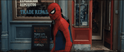 A Man In A Spiderman Costume Stands In Front Of A Sign That Says Reparacion Repuestos Trade R. GIF