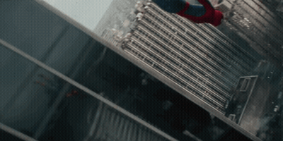 A Man In A Spiderman Suit Is Flying Through The Air Between Two Tall Buildings GIF