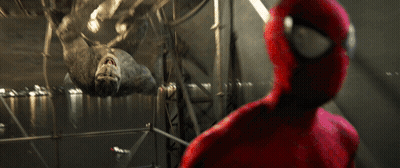 A Man In A Spiderman Suit Looks At A Large Spider GIF
